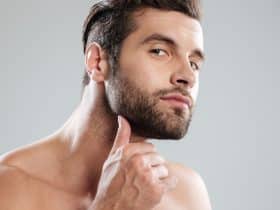portrait of handsome naked bearded man examining his face