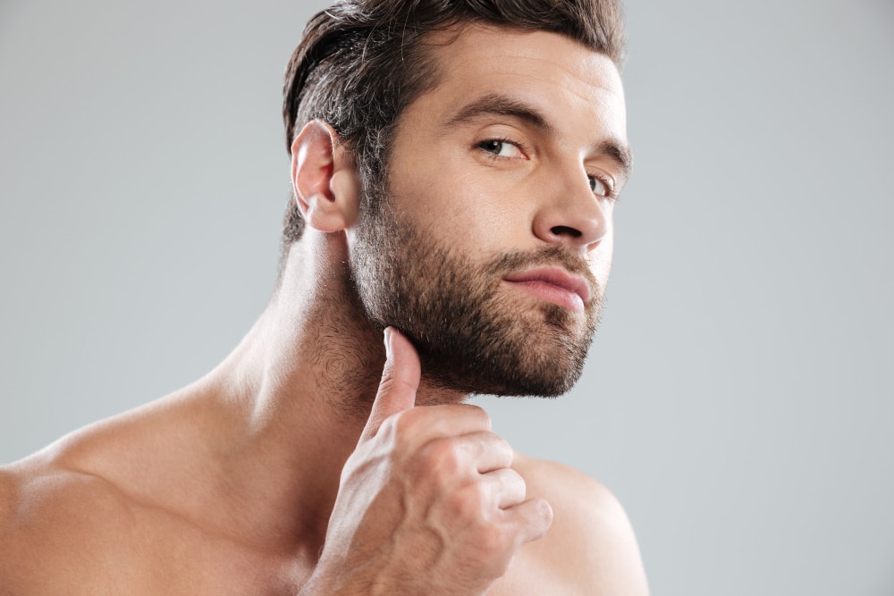 portrait of handsome naked bearded man examining his face